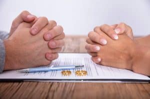 Couple's Hand With Divorce Agreement And Wedding Rings